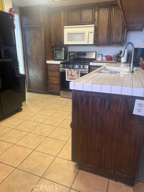 kitchen featuring dark brown cabinetry, tile counters, sink, and stainless steel gas stove