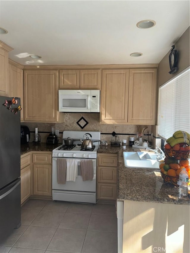 kitchen with tile patterned floors, sink, dark stone countertops, light brown cabinets, and white appliances