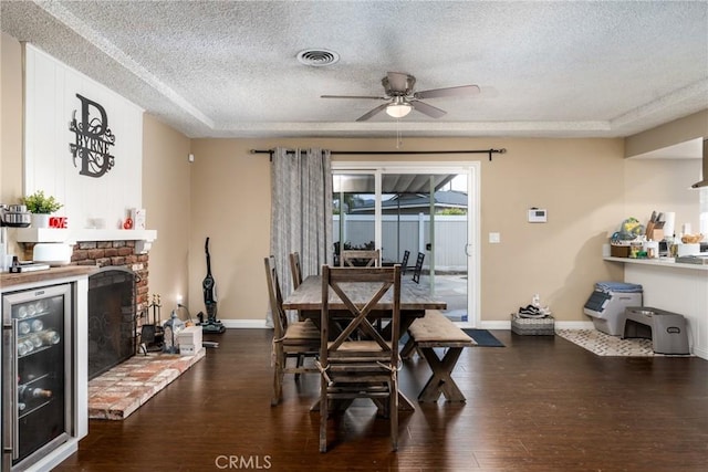 dining space featuring a brick fireplace, dark hardwood / wood-style floors, beverage cooler, and a textured ceiling