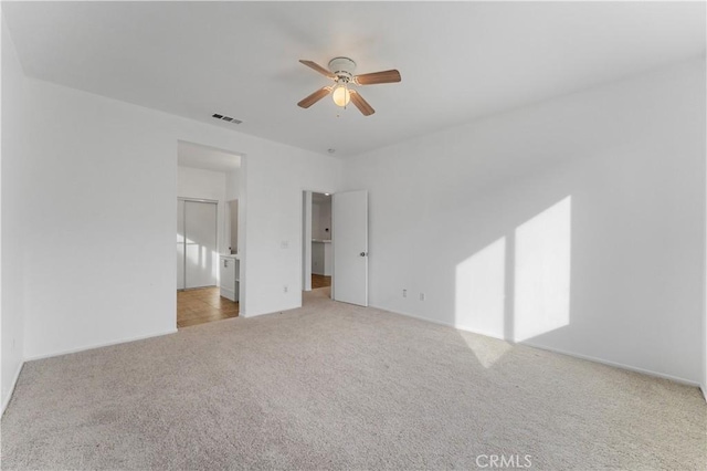 unfurnished bedroom featuring visible vents, a spacious closet, a ceiling fan, light carpet, and connected bathroom