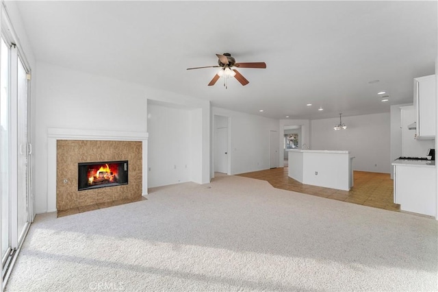 unfurnished living room with light carpet, a tiled fireplace, and ceiling fan