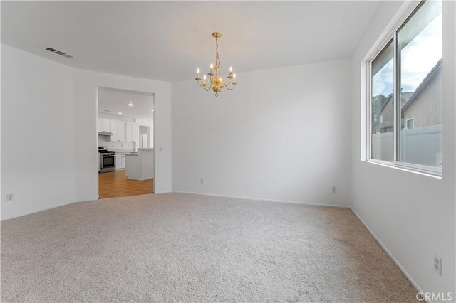 spare room featuring light carpet and a notable chandelier