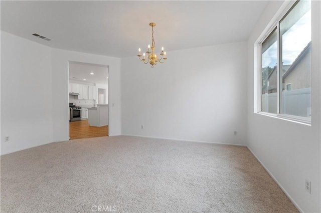 empty room featuring light carpet, visible vents, and an inviting chandelier