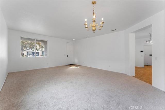 carpeted spare room with visible vents and a notable chandelier