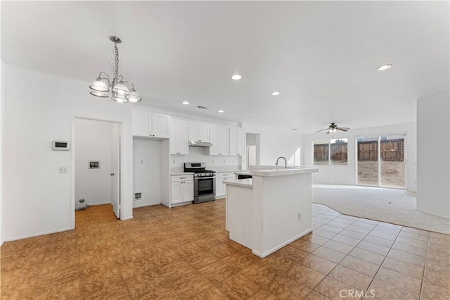 kitchen with ceiling fan with notable chandelier, stainless steel stove, decorative light fixtures, white cabinetry, and a kitchen island with sink