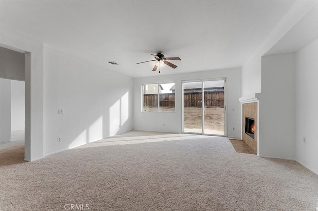 unfurnished living room featuring a tiled fireplace, light colored carpet, and ceiling fan