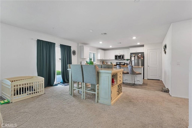 kitchen with a breakfast bar area, a kitchen island, light colored carpet, stainless steel appliances, and white cabinets