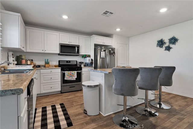 kitchen with dark wood-type flooring, sink, a center island, stainless steel appliances, and white cabinets