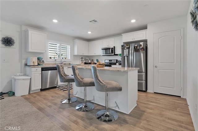 kitchen with a kitchen bar, light hardwood / wood-style flooring, appliances with stainless steel finishes, a kitchen island, and white cabinets