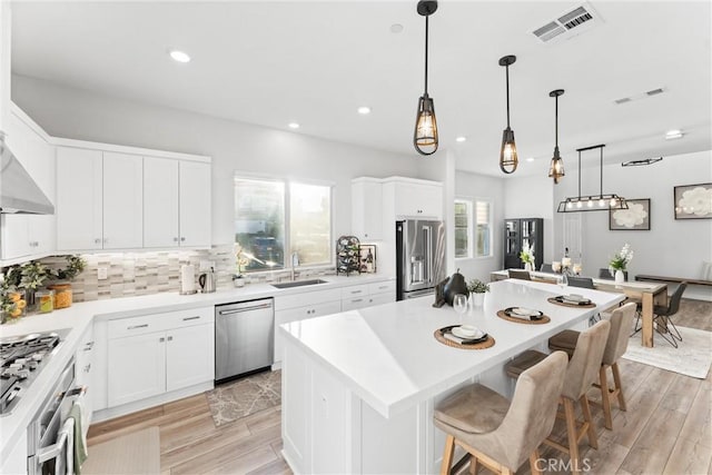 kitchen with pendant lighting, sink, appliances with stainless steel finishes, a center island, and white cabinets