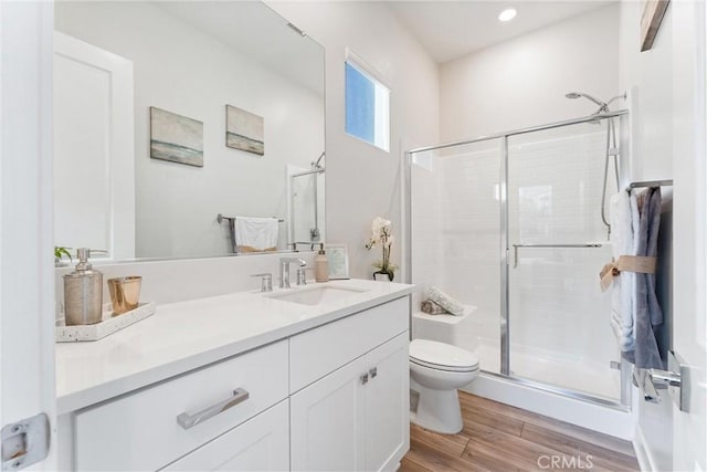 bathroom featuring hardwood / wood-style flooring, vanity, a shower with shower door, and toilet