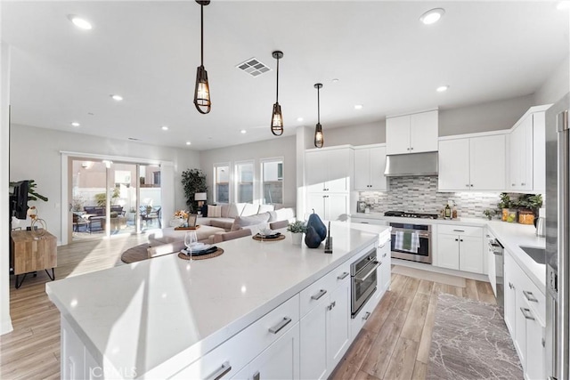 kitchen featuring white cabinetry, a center island, hanging light fixtures, stainless steel appliances, and backsplash