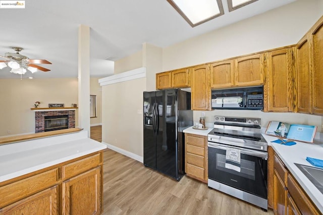 kitchen featuring sink, ceiling fan, a fireplace, black appliances, and light hardwood / wood-style floors