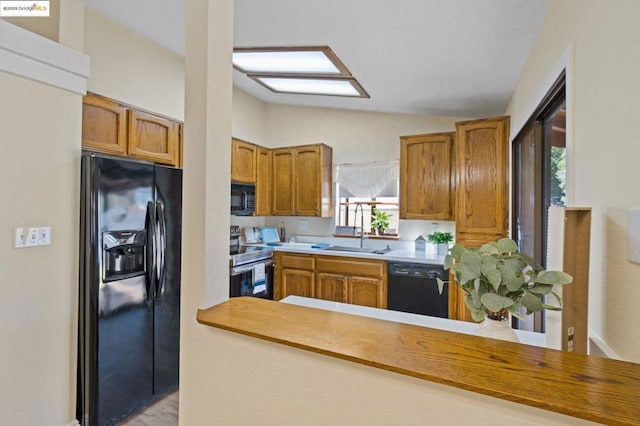 kitchen featuring lofted ceiling, sink, kitchen peninsula, and black appliances