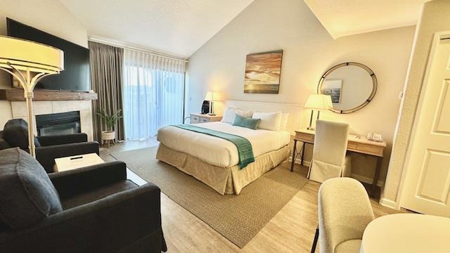 bedroom with a tiled fireplace, vaulted ceiling, and wood-type flooring