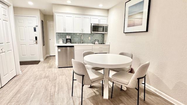 kitchen featuring sink, appliances with stainless steel finishes, white cabinets, decorative backsplash, and light wood-type flooring