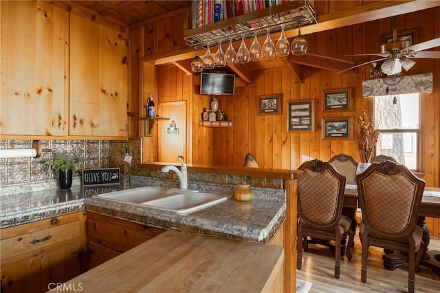 kitchen with ceiling fan, wooden walls, light hardwood / wood-style floors, and sink