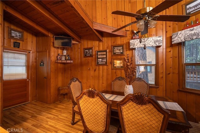 dining area featuring wooden walls, beam ceiling, and light wood-type flooring