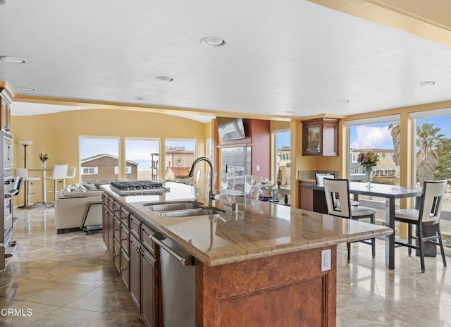 kitchen with light stone countertops, an island with sink, appliances with stainless steel finishes, and sink