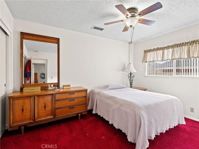 bedroom featuring ceiling fan, dark carpet, a closet, and a textured ceiling