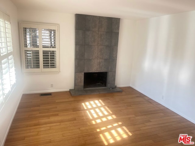 unfurnished living room with a healthy amount of sunlight, a tiled fireplace, and hardwood / wood-style floors