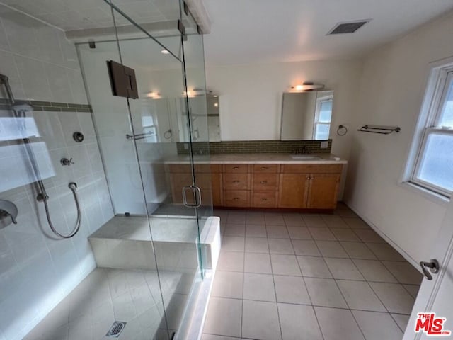 bathroom with tile patterned floors, vanity, a shower with door, and backsplash