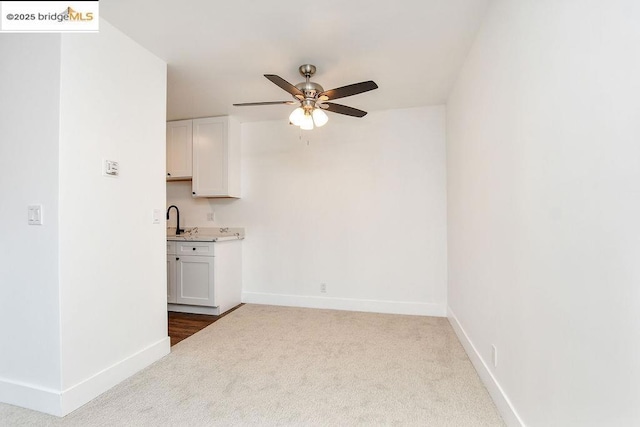 kitchen featuring sink, light carpet, white cabinets, and ceiling fan