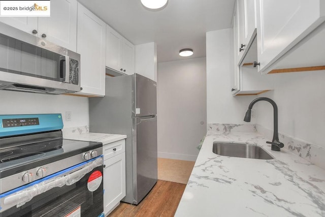 kitchen featuring sink, white cabinets, stainless steel appliances, light stone countertops, and light hardwood / wood-style flooring