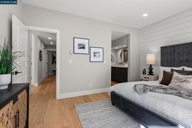 bedroom featuring wooden walls, ensuite bath, and light hardwood / wood-style flooring