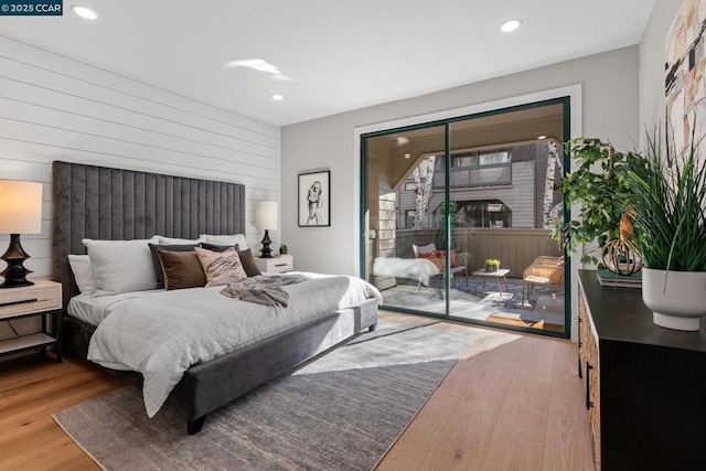 bedroom featuring access to exterior, light hardwood / wood-style flooring, and wood walls