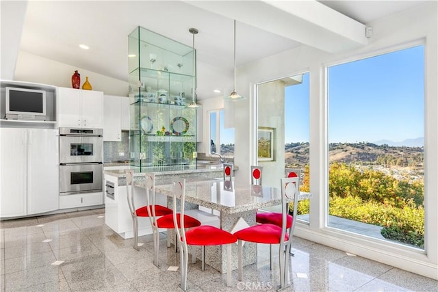 kitchen with pendant lighting, double oven, backsplash, white cabinets, and light stone counters