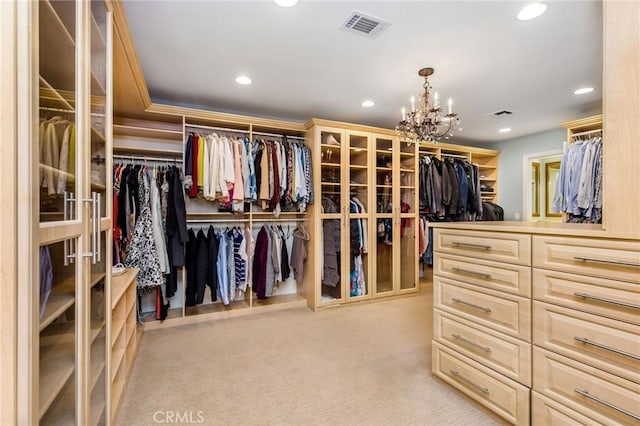 walk in closet with light colored carpet and a chandelier