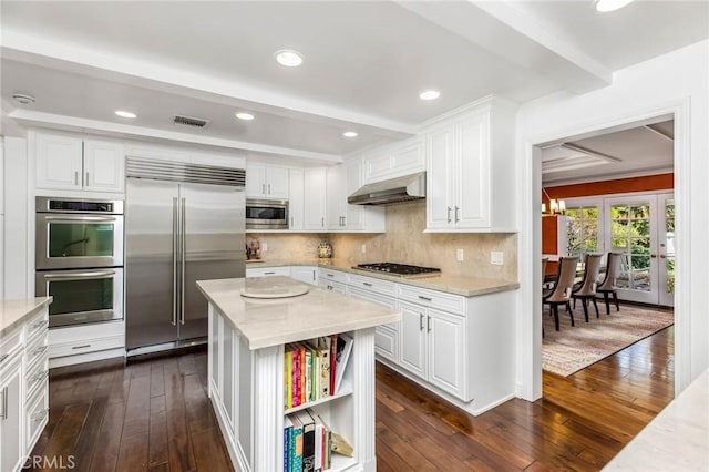 kitchen with light stone counters, built in appliances, and white cabinets