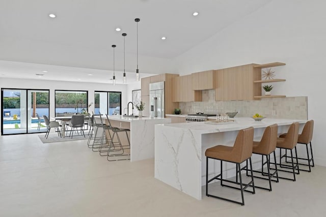 kitchen with pendant lighting, stainless steel built in refrigerator, backsplash, a large island with sink, and light stone counters