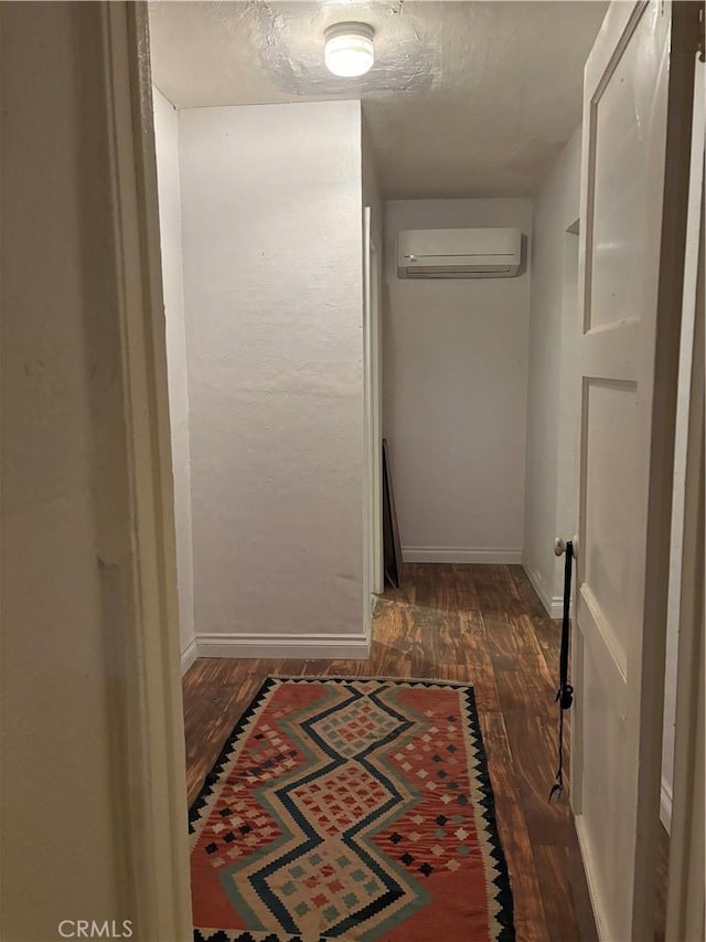 hallway featuring dark wood-style floors, an AC wall unit, a textured ceiling, and baseboards