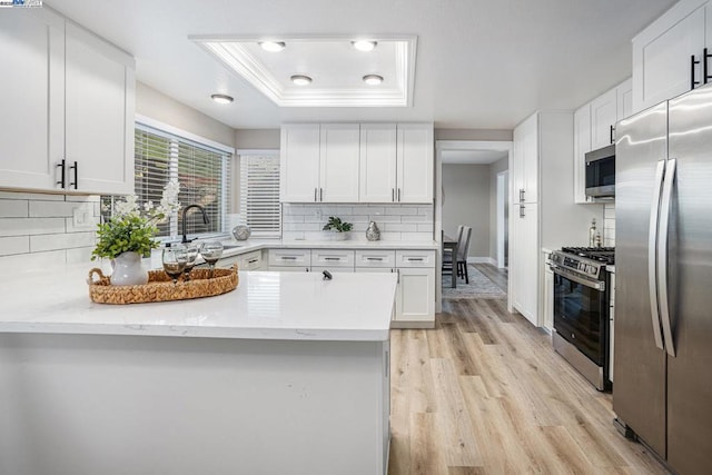 kitchen featuring appliances with stainless steel finishes, white cabinetry, sink, a tray ceiling, and light wood-type flooring