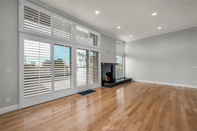 unfurnished living room featuring recessed lighting, baseboards, hardwood / wood-style floors, and a warm lit fireplace