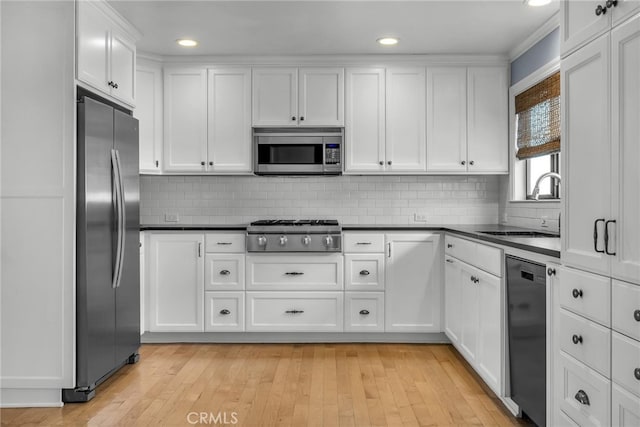kitchen with white cabinets, dark countertops, a sink, stainless steel appliances, and backsplash