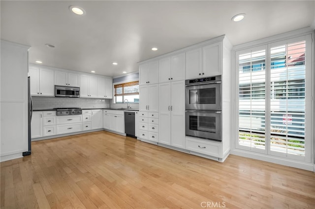 kitchen featuring light wood-type flooring, white cabinets, appliances with stainless steel finishes, dark countertops, and decorative backsplash
