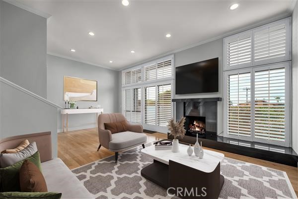 living area featuring recessed lighting, wood finished floors, a warm lit fireplace, and ornamental molding