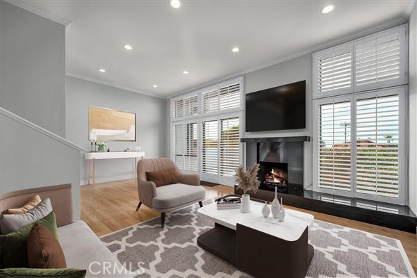 living area featuring wood finished floors, ornamental molding, a warm lit fireplace, and recessed lighting