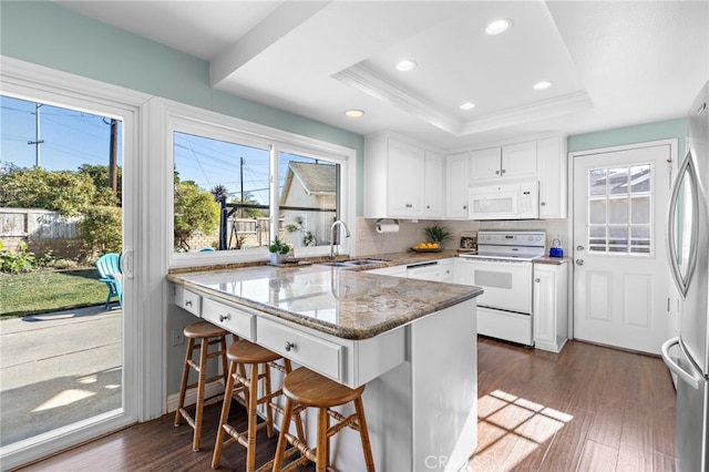 kitchen featuring sink, white appliances, a breakfast bar, white cabinets, and kitchen peninsula