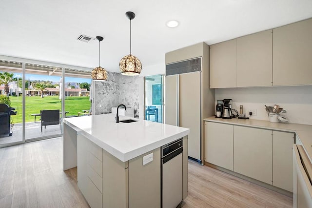 kitchen with decorative light fixtures, an island with sink, sink, paneled built in refrigerator, and light hardwood / wood-style floors