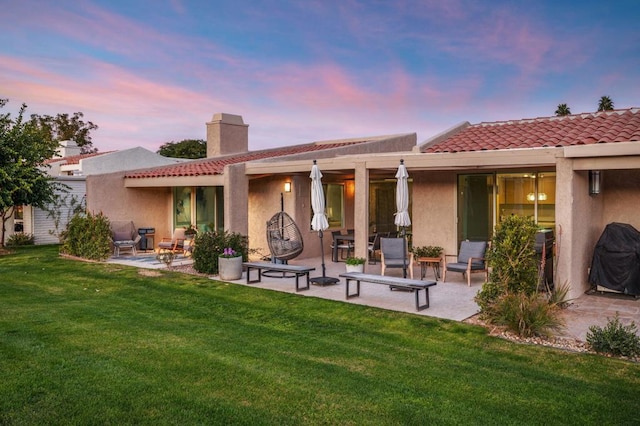 back house at dusk with a lawn and a patio area