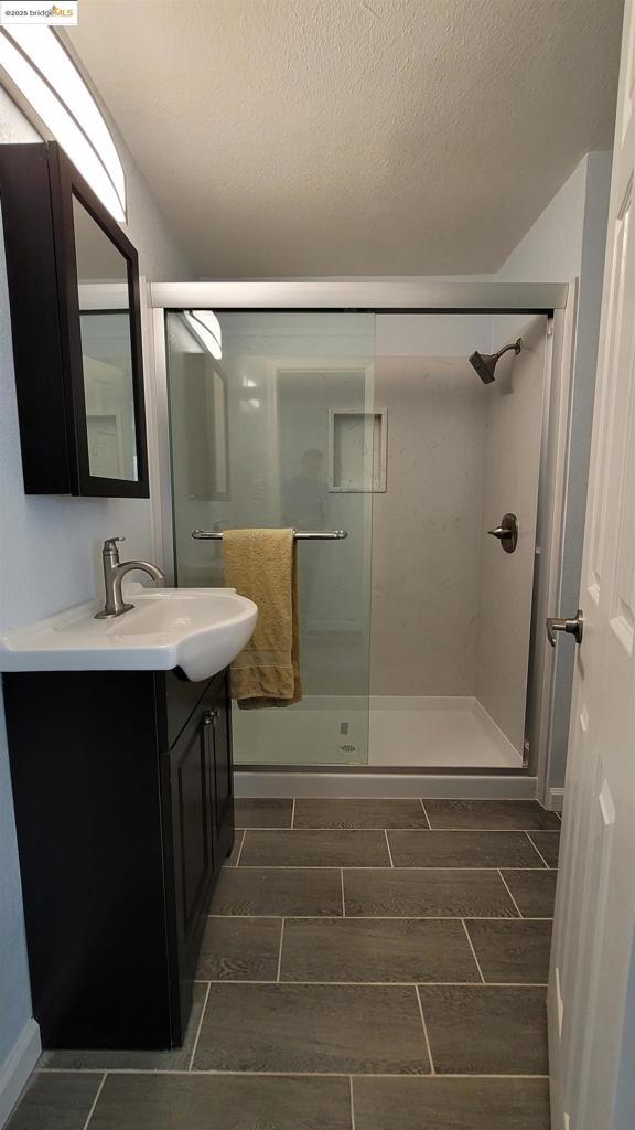 bathroom with vanity, a shower with shower door, and a textured ceiling