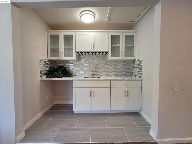 kitchen with sink, light tile patterned floors, backsplash, light stone countertops, and white cabinets