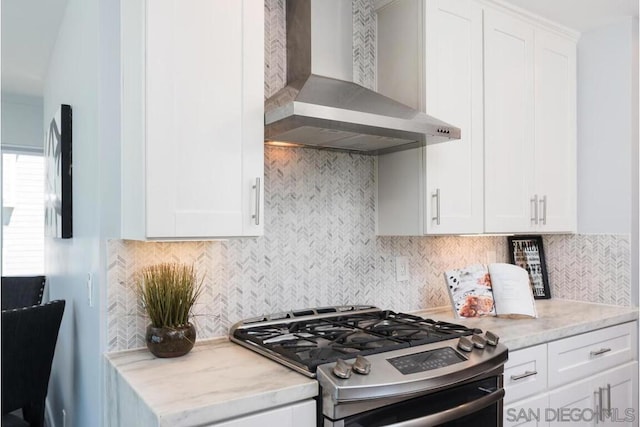 kitchen featuring gas range, wall chimney range hood, white cabinets, and backsplash