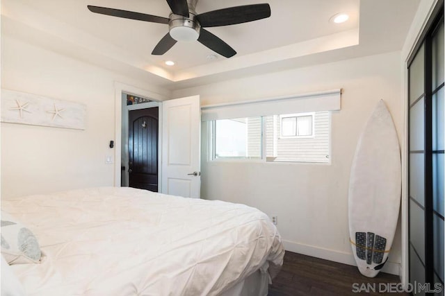 bedroom with dark hardwood / wood-style flooring, a tray ceiling, and ceiling fan