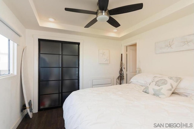 bedroom with a tray ceiling, dark hardwood / wood-style floors, and ceiling fan