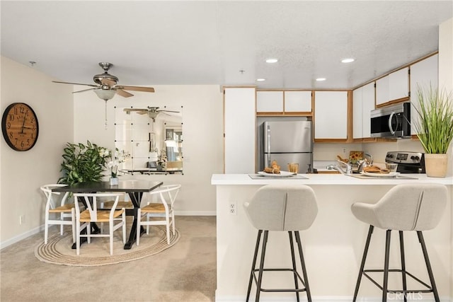 kitchen featuring ceiling fan, stainless steel appliances, white cabinets, a kitchen bar, and light colored carpet